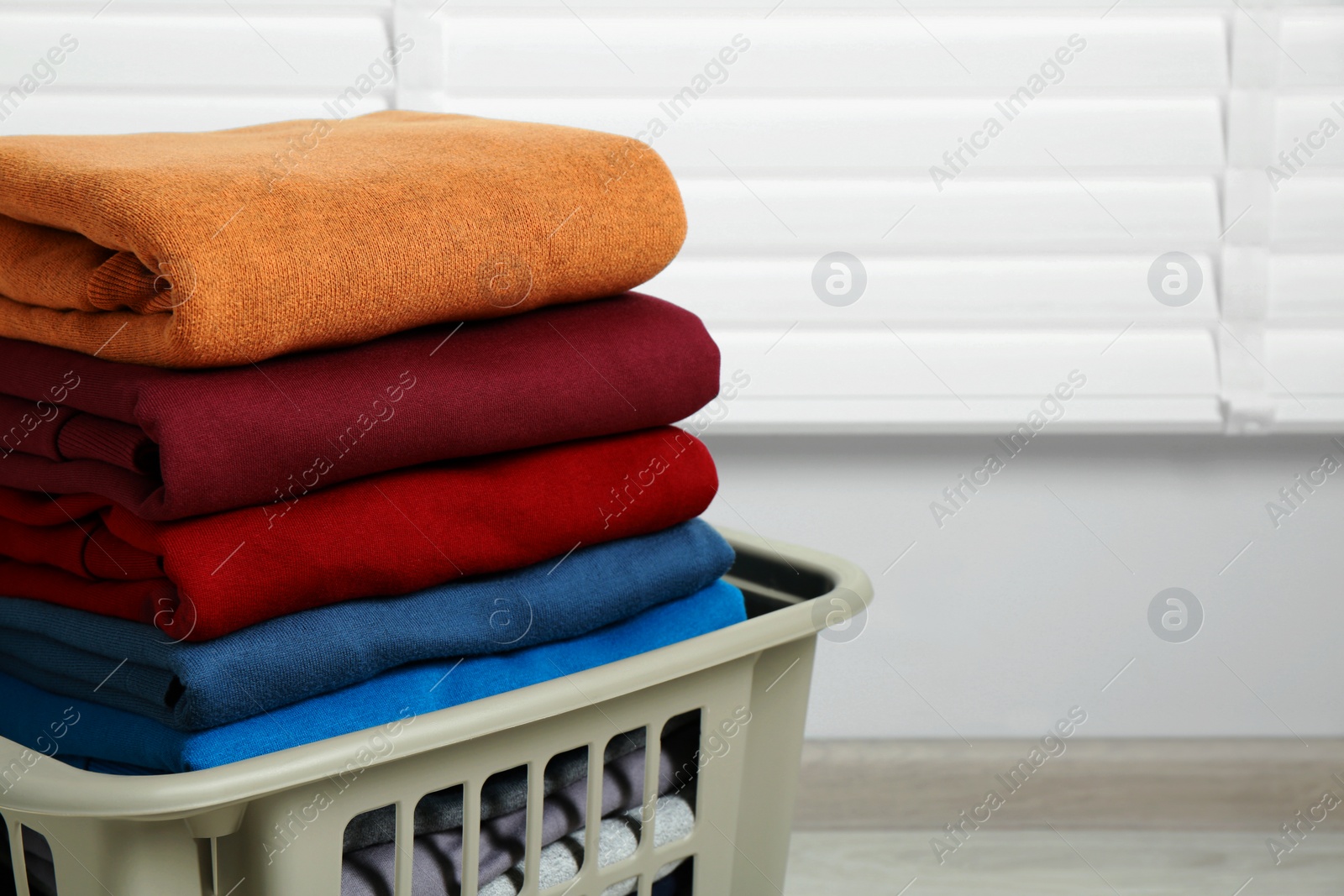 Photo of Plastic laundry basket with clean clothes indoors, closeup. Space for text