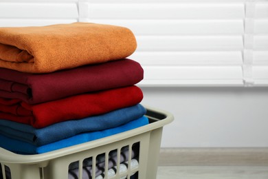 Photo of Plastic laundry basket with clean clothes indoors, closeup. Space for text