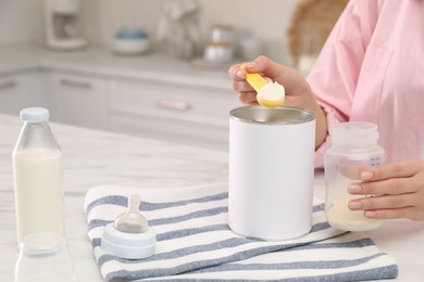 Photo of Woman preparing infant formula at table indoors, closeup. Baby milk