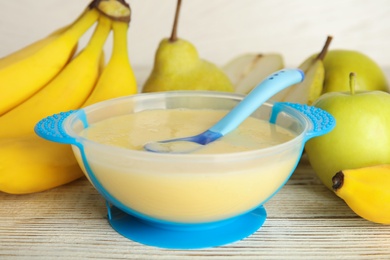 Baby food in bowl and fresh ingredients on white wooden table