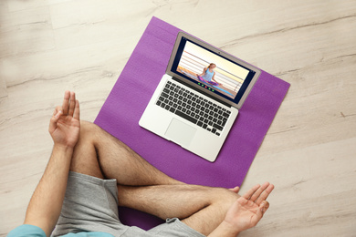 Image of Distance yoga course during coronavirus pandemic. Man having online practice with instructor via laptop at home, top view