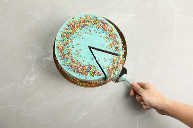 Woman taking slice of fresh delicious birthday cake at table, top view