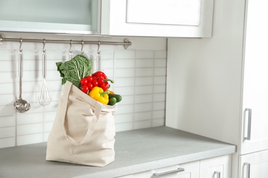 Photo of Textile shopping bag full of vegetables on countertop in kitchen. Space for text