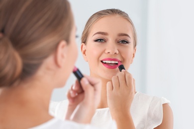 Beautiful young woman applying lipstick in front of mirror