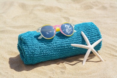Photo of Towel, stylish sunglasses and starfish on sand outdoors. Beach accessories