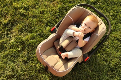 Photo of Adorable baby in child safety seat on green grass