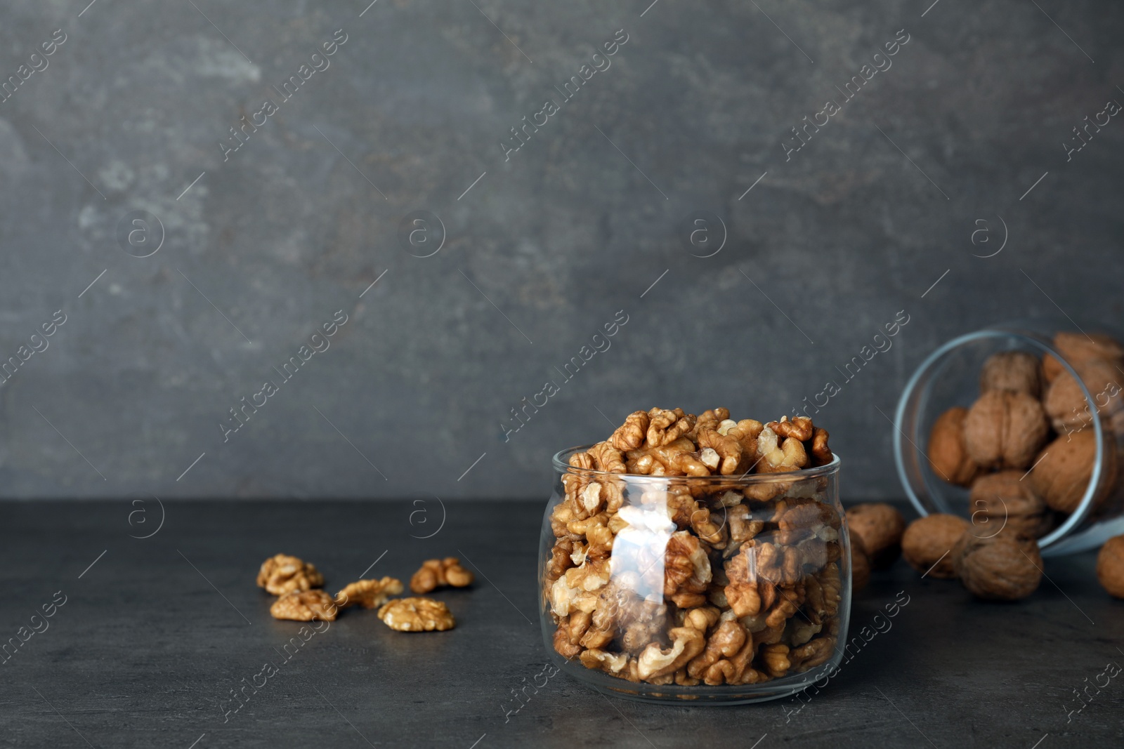 Photo of Glass jar with walnuts on table against grey background. Space for text