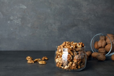 Glass jar with walnuts on table against grey background. Space for text