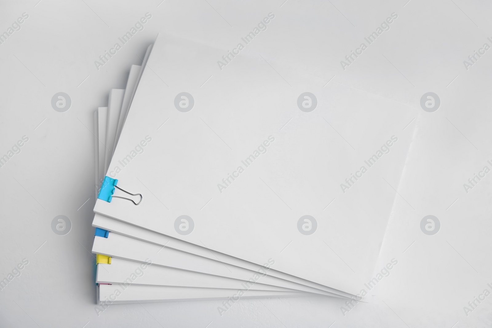 Photo of Many sheets of paper with colorful clips on white background, top view