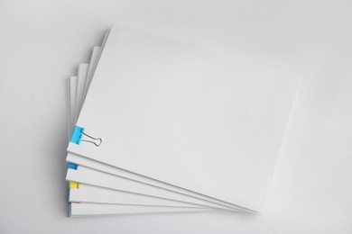 Photo of Many sheets of paper with colorful clips on white background, top view