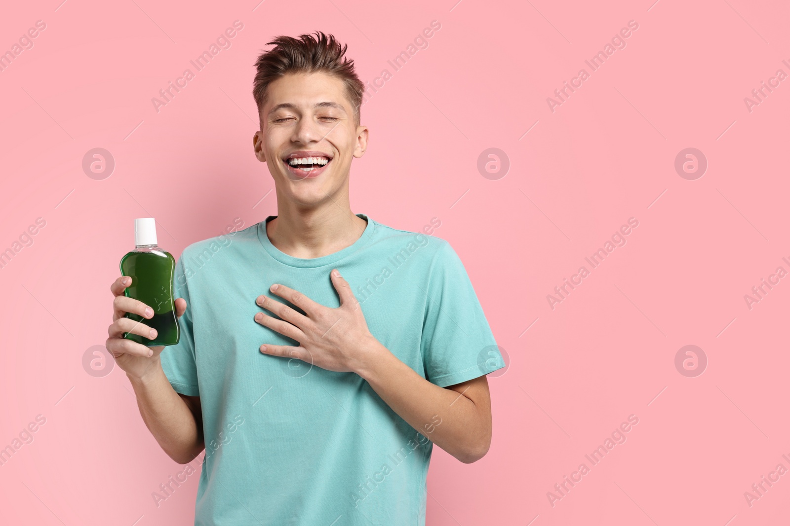 Photo of Young man with mouthwash on pink background, space for text