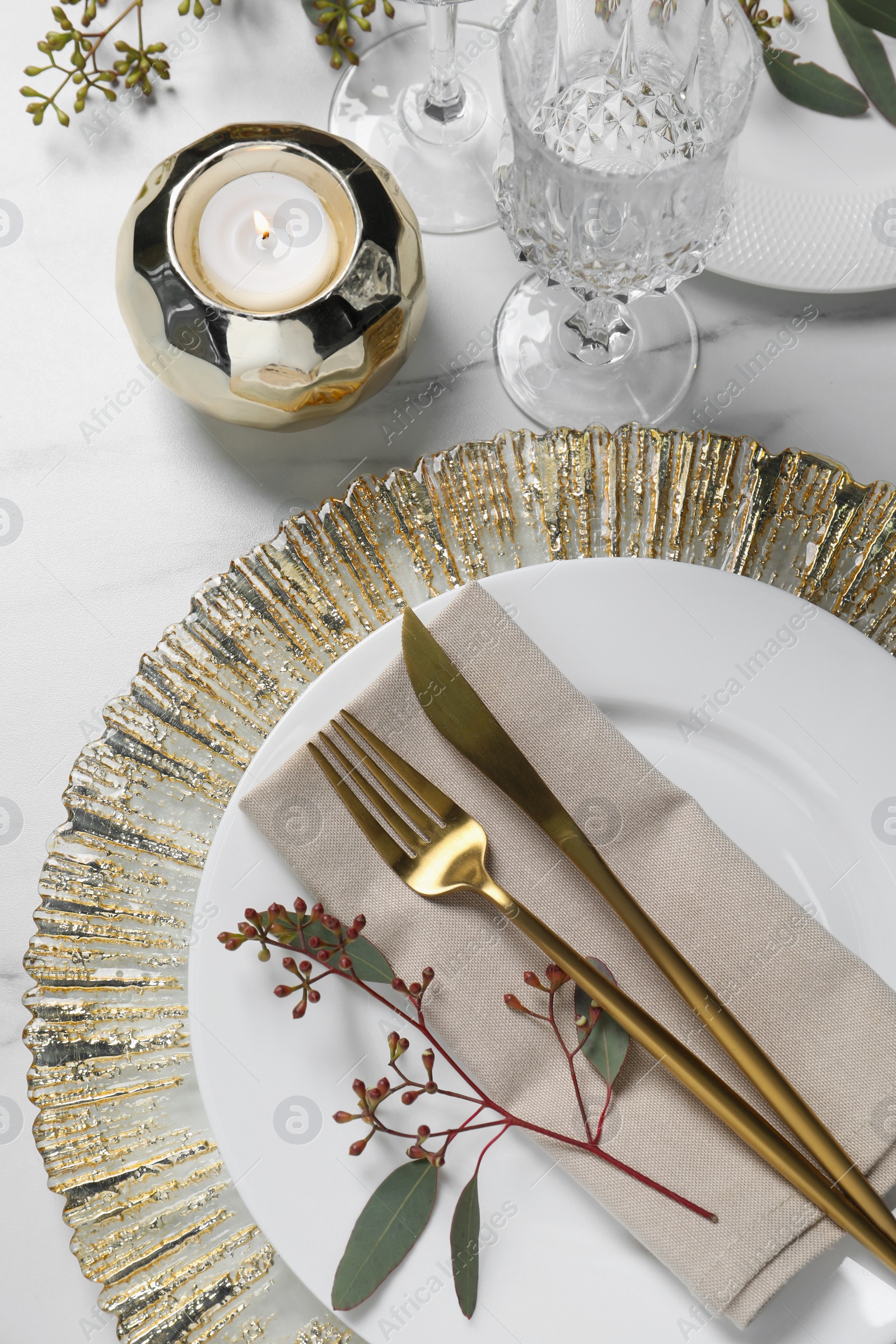 Photo of Stylish setting with cutlery, burning candle and eucalyptus leaves on white marble table, flat lay