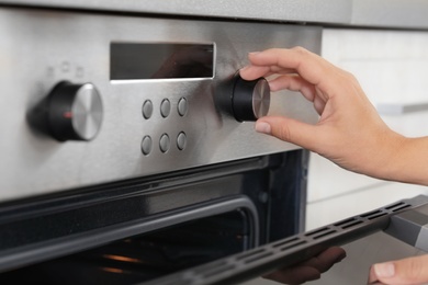 Woman regulating cooking mode on oven panel, closeup