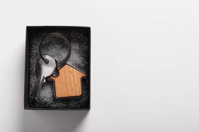 Key with trinket in shape of house and gift box on light grey background, top view with space for text. Housewarming party