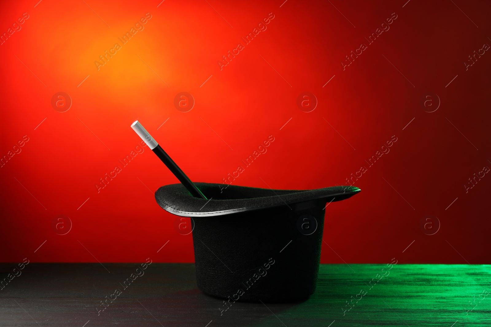 Photo of Magician's hat and wand on black wooden table against color background