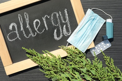 Photo of Ragweed plant (Ambrosia genus) medication and chalkboard with word "ALLERGY" on dark grey table, flat lay
