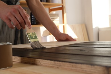 Photo of Man with brush applying wood stain onto wooden surface indoors, closeup