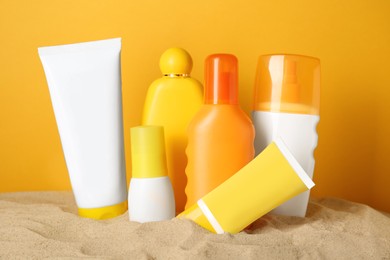 Photo of Many different suntan products on sand against orange background