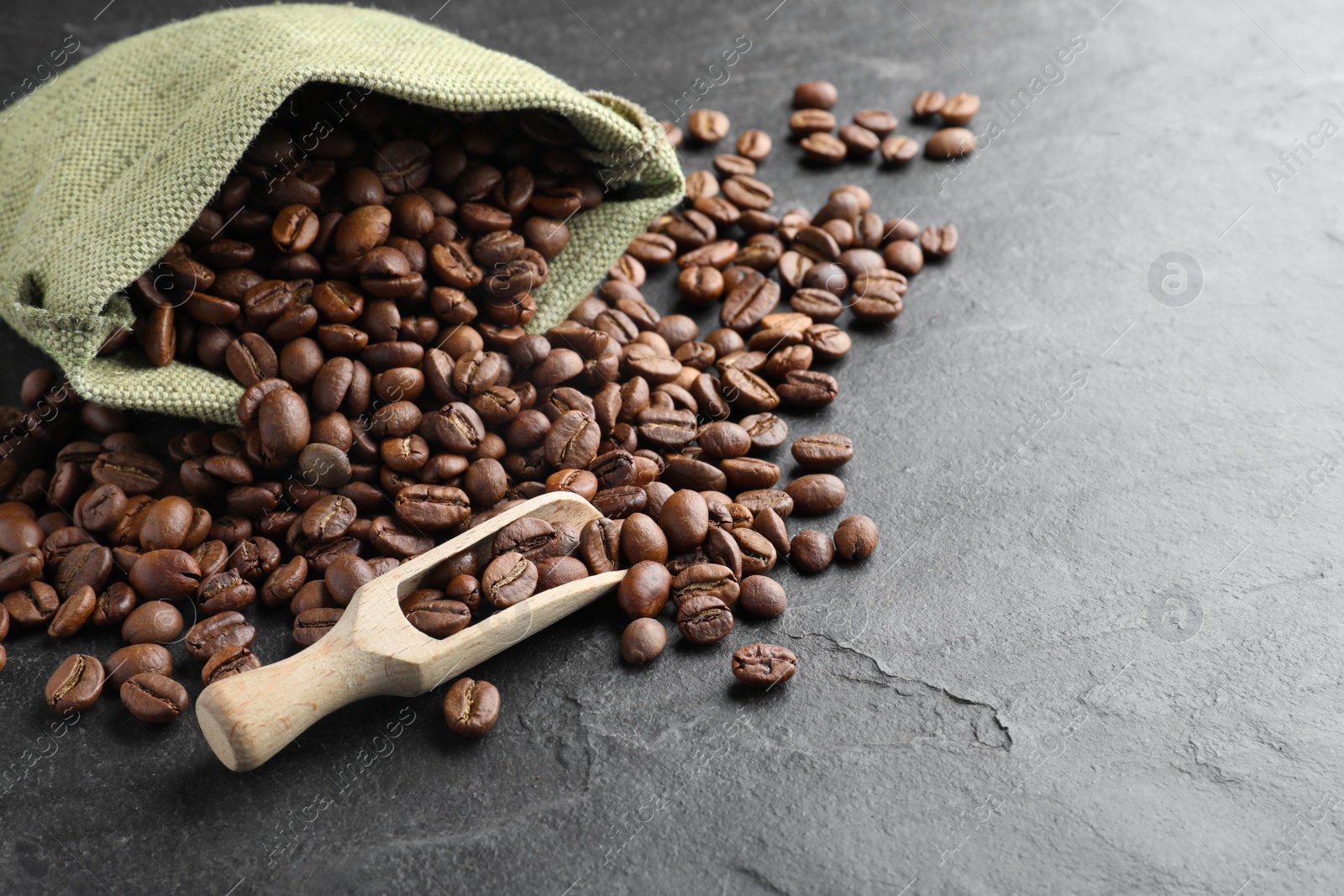 Photo of Bag and wooden scoop with roasted coffee beans on black table. Space for text