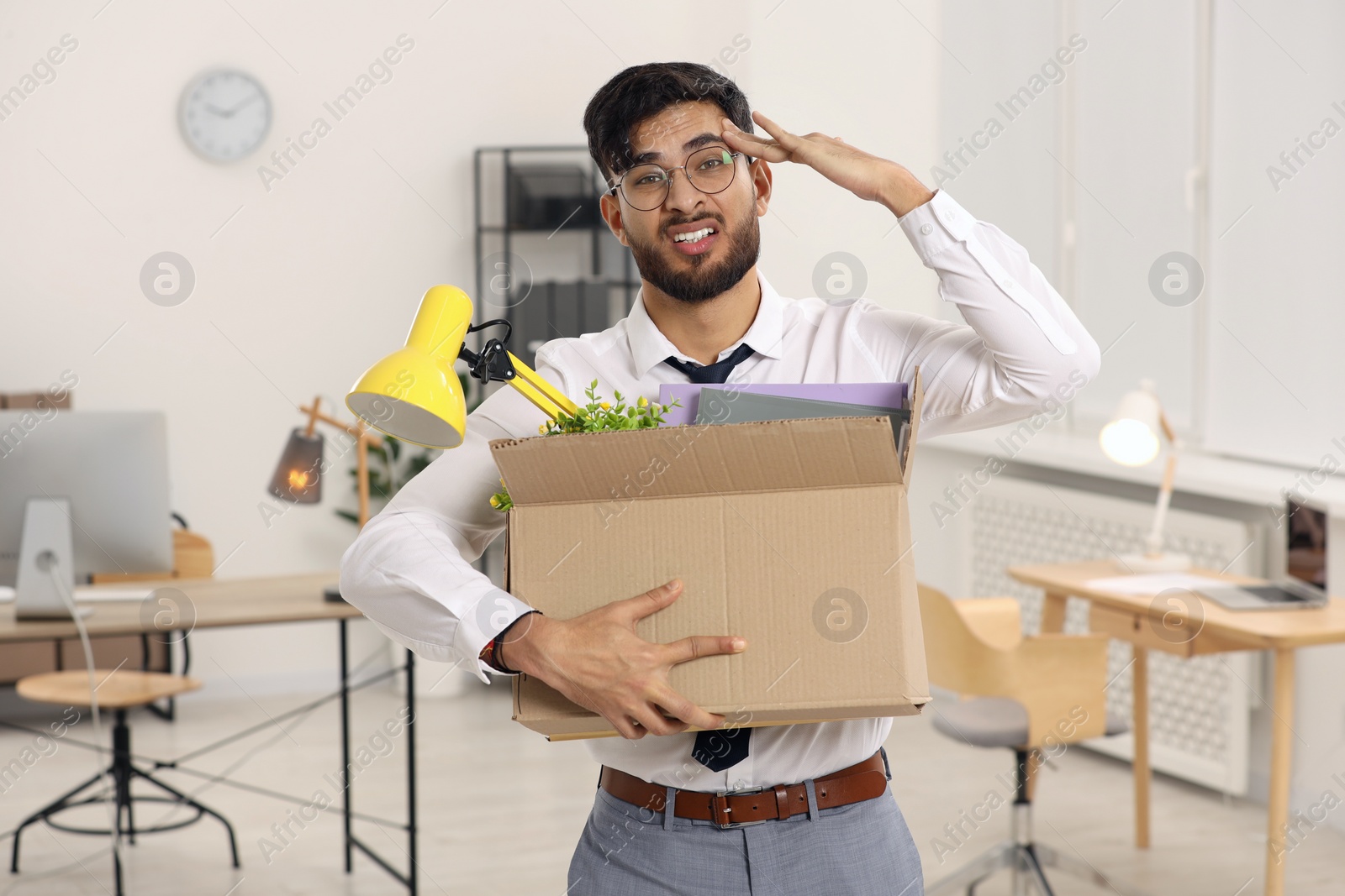 Photo of Unemployment problem. Frustrated man with box of personal belongings in office