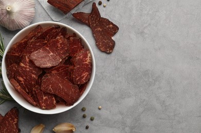 Delicious beef jerky in bowl and seasoning on light gray table, flat lay. Space for text