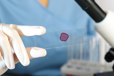 Scientist holding microscope slide with red sample in laboratory, closeup