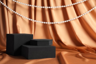 Photo of Black geometric figures and pearls on light brown fabric, space for text. Stylish presentation for product