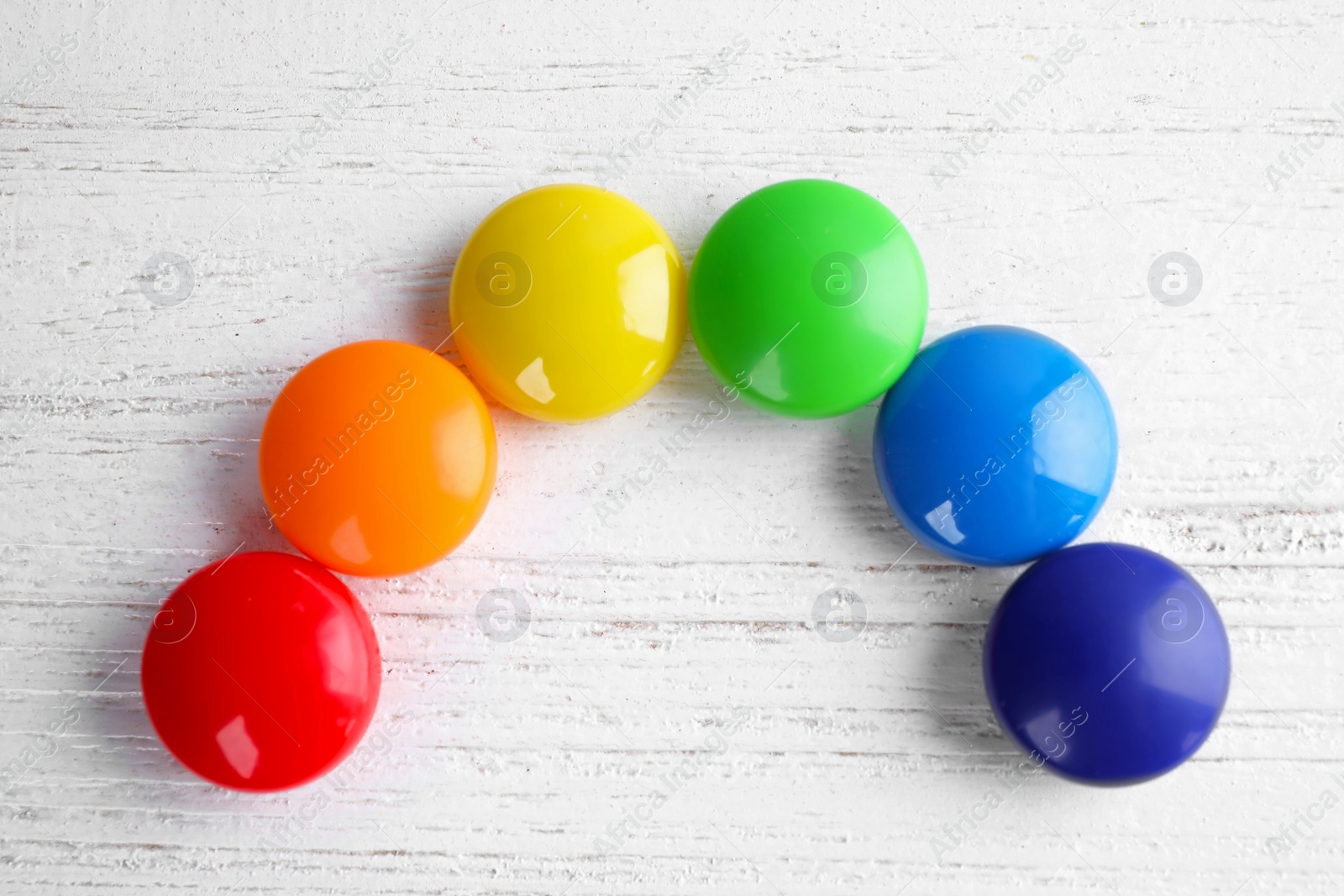 Photo of Bright magnets on white wooden background, flat lay. Rainbow colors