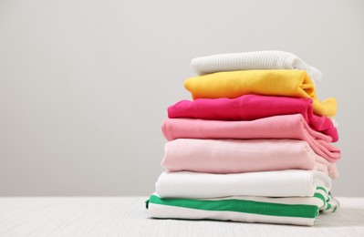 Photo of Stack of folded clothes on wooden table against beige background, space for text