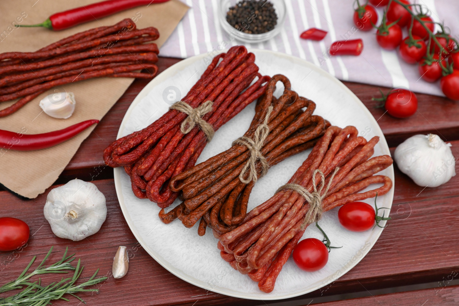 Photo of Bundles of delicious kabanosy with rosemary, tomatoes, chilli and garlic on wooden table, above view