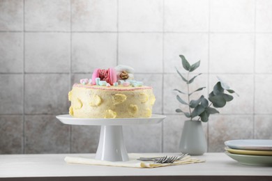 Photo of Delicious cake decorated with macarons and marshmallows served on white wooden table near tiled wall