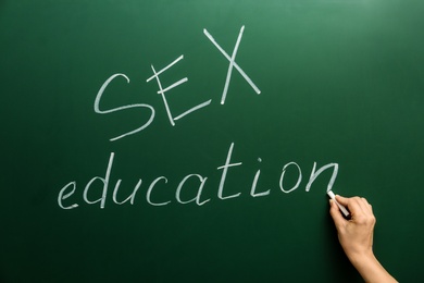 Photo of Woman writing phrase "SEX EDUCATION" on green chalkboard