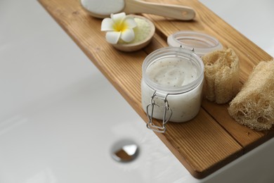 Wooden tray with spa products and plumeria flower on bath tub, closeup