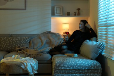 Woman with glass of wine resting on couch in room at night