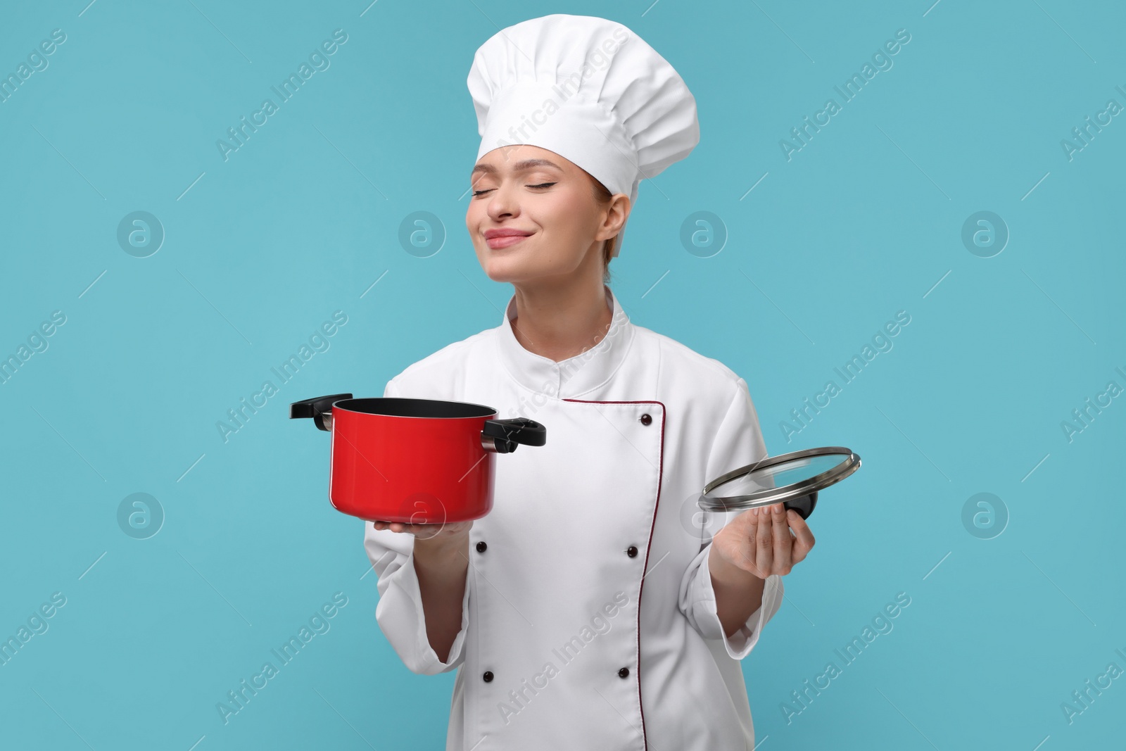 Photo of Happy woman chef in uniform holding cooking pot on light blue background