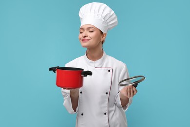 Happy woman chef in uniform holding cooking pot on light blue background