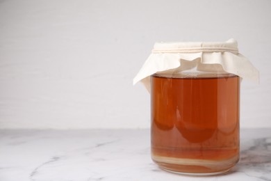 Photo of Tasty kombucha in glass jar on white marble table, space for text