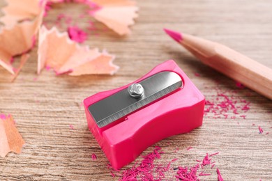 Photo of Pink sharpener, pencil and shavings on wooden table, closeup