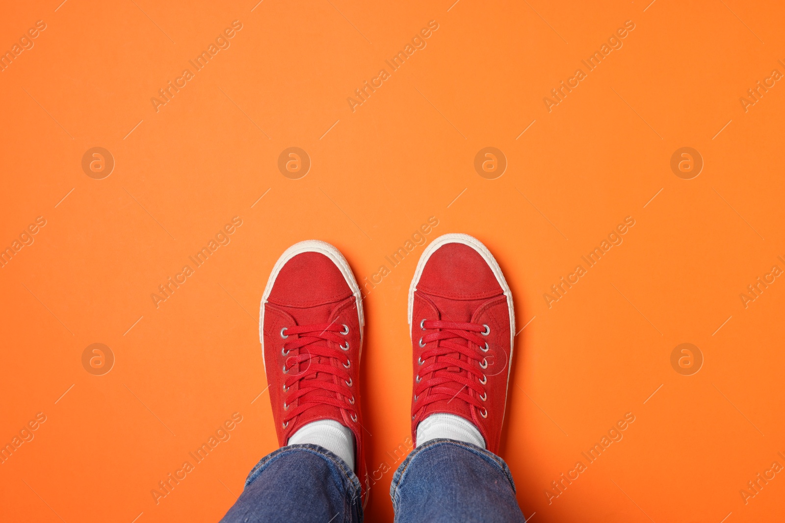 Photo of Woman in stylish sneakers on orange background, top view. Space for text