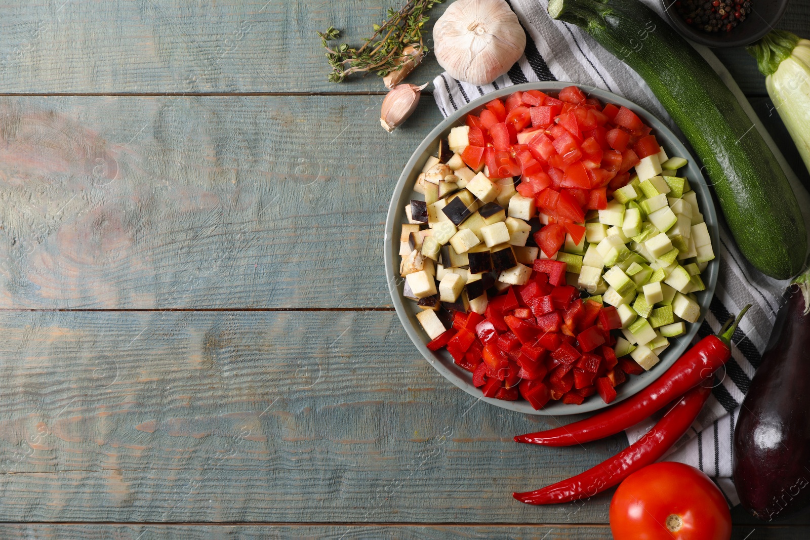 Photo of Cooking delicious ratatouille. Fresh ripe vegetables and plate on light blue wooden table, flat lay. Space for text