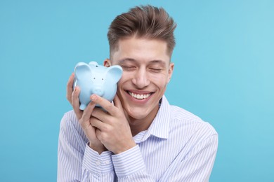 Photo of Happy man with piggy bank on light blue background