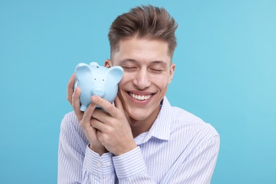 Happy man with piggy bank on light blue background