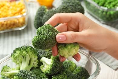 Woman putting broccoli into glass container at table, closeup. Food storage