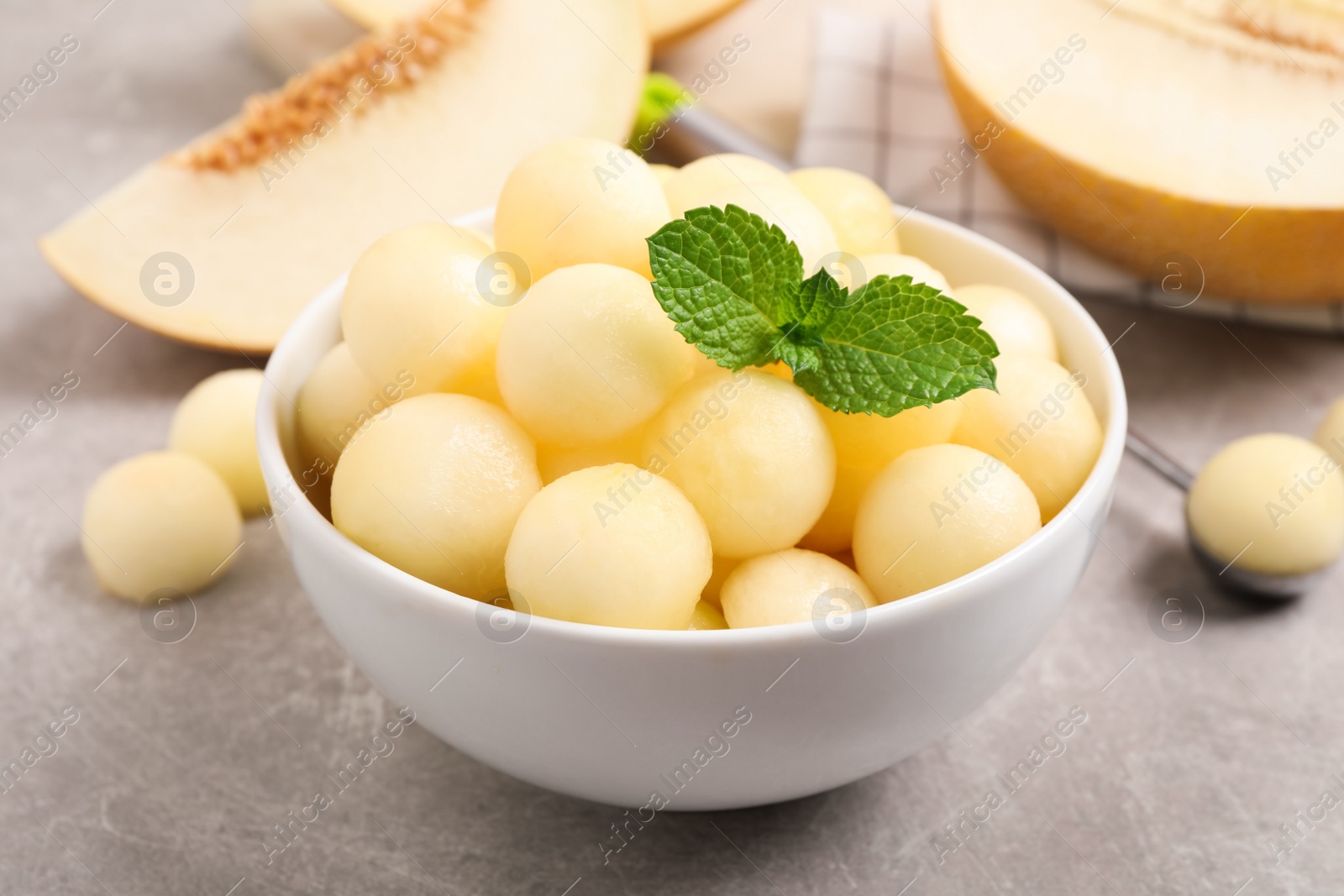 Photo of Melon balls and mint in bowl on light grey table, closeup