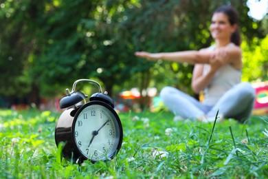 Photo of Young woman doing morning exercise in park, focus on alarm clock