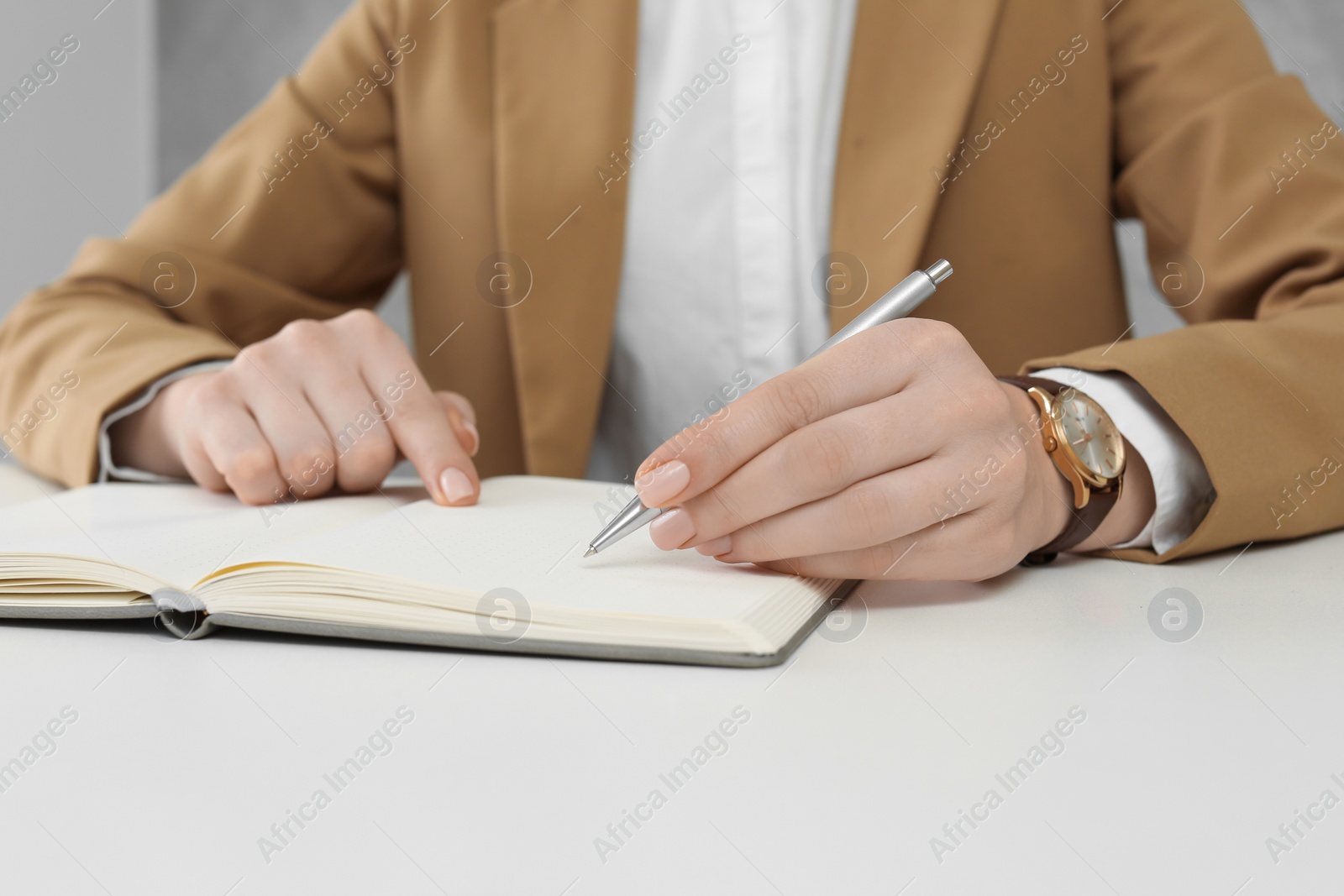 Photo of Woman writing in notebook at white table, closeup