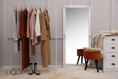 Rack with different stylish clothes and shoes near grey wall in room