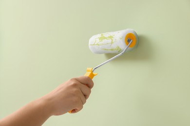 Worker using roller to paint wall with pale olive dye, closeup