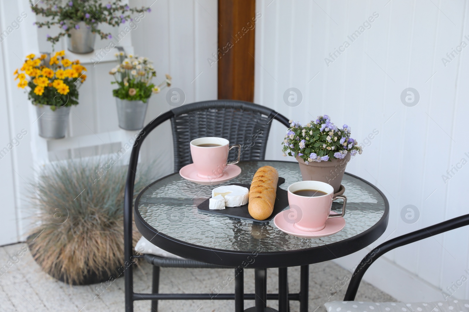 Photo of Cups of coffee, potted plant, bread and cheese on glass table. Relaxing place at outdoor terrace