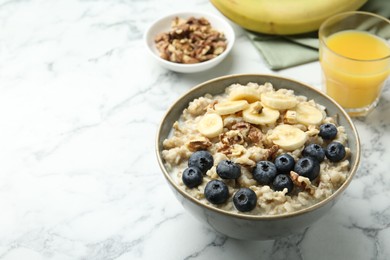 Tasty oatmeal with banana, blueberries, walnuts and milk served in bowl on white marble table, space for text